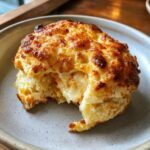 A close-up of a golden-brown shrimp and crab biscuit melt, with gooey cheese oozing out from the center.
