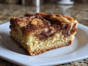 A single square of moist snickerdoodle blondies with a rich cinnamon swirl topping served on a white plate.
