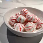 A white bowl filled with soft Christmas peppermints, featuring red and green stripes.