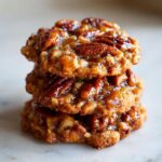 A close-up stack of three gooey, glazed pecan pie cookies topped with whole pecans.
