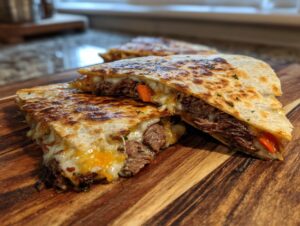 Close-up of a golden-brown steak and cheese quesadilla, sliced and showing melted cheese, tender steak, and red pepper.