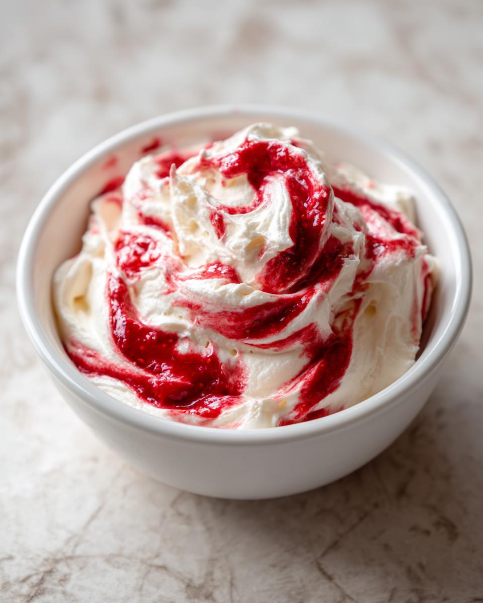 A close-up of creamy strawberry cheesecake dip swirled with bright red strawberry sauce in a white bowl.