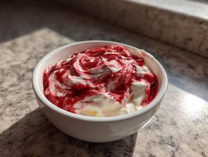 A white bowl filled with creamy strawberry cheesecake dip swirled with bright red strawberry topping.