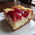 A delicious slice of strawberry dump cheesecake on a white plate, showcasing the creamy filling and fresh strawberry topping.