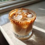 A close-up of a Toasted Coconut White Russian cocktail with ice and a rim of toasted coconut flakes.