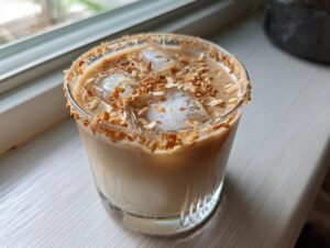 A close-up of a Toasted Coconut White Russian cocktail in a glass, rimmed with toasted coconut and filled with ice.