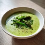 A close-up of creamy, vibrant green asparagus soup garnished with cooked asparagus tips and black pepper.