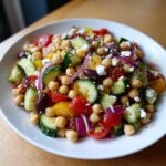 Close-up of a vibrant mediterranean chickpea salad featuring chickpeas, cucumbers, tomatoes, red onion, olives, and feta.