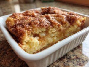 A close-up view of a freshly baked snickerdoodle cobbler slice topped with cinnamon sugar in a white ramekin.