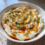 A bowl of fluffy whipped ricotta dip topped with golden honey and finely chopped green chives.