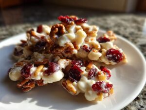 Close-up of white chocolate cranberry pecan clusters on a white plate, showcasing the sweet and crunchy treat.