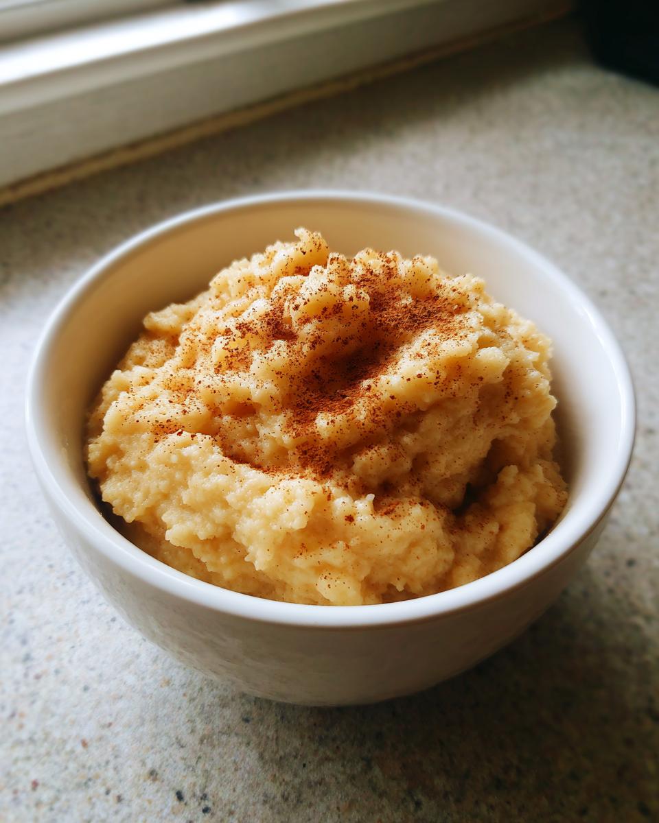 A close-up of chunky, homemade applesauce topped generously with ground cinnamon in a white bowl.