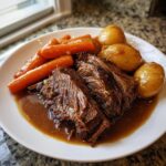 Two slices of tender, shredded pot roast served with glazed carrots and small potatoes in rich brown gravy.