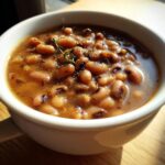 Close-up of a white bowl filled with a savory black eyed peas recipe, garnished with pepper and thyme.