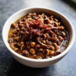 A white bowl filled with rich, savory black eyed peas topped with shredded smoked meat.