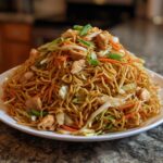 A large mound of delicious chicken chow mein recipe featuring noodles, chicken pieces, carrots, and cabbage.