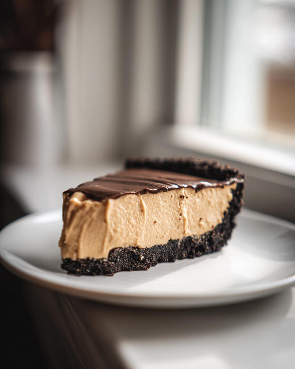 A thick slice of peanut butter pie with a dark chocolate crust and ganache topping on a white plate.