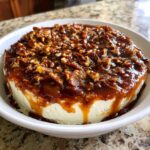 A round block of cream cheese covered in rich caramel sauce and chopped pecans, ready to serve as pecan pie dip.