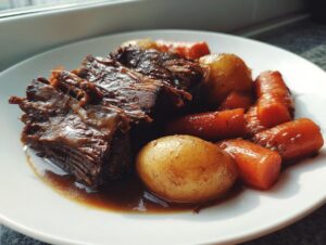 A serving of tender, shredded pot roast with glazed carrots and small potatoes in rich gravy.