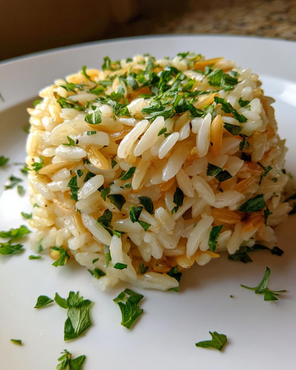 Close-up of a perfectly molded serving of fluffy rice pilaf mixed with toasted pasta, topped with fresh chopped parsley.