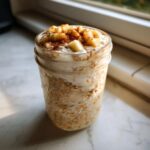 Close-up of apple cinnamon overnight oats layered in a mason jar, topped with yogurt, diced apples, and cinnamon.