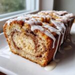 Close-up of a moist slice of apple fritter bread showing cinnamon swirl and vanilla glaze dripping down.