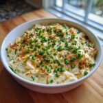 A white bowl filled with rich, creamy baked onion dip, topped with melted cheese and fresh green chives.