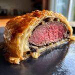 Close-up of a perfectly cooked beef wellington recipe slice showing medium-rare center and flaky pastry.