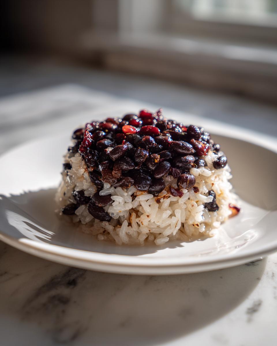A molded serving of white rice topped generously with glossy black beans and rice mixture.