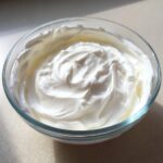 A clear glass bowl filled with thick, bright white, freshly whipped cookie icing.