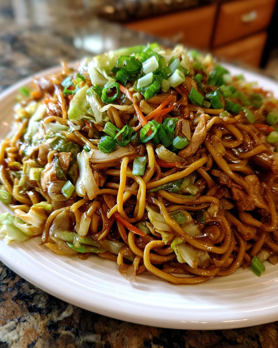 Close-up of a plate piled high with saucy chicken chow mein recipe noodles, vegetables, and green onions.