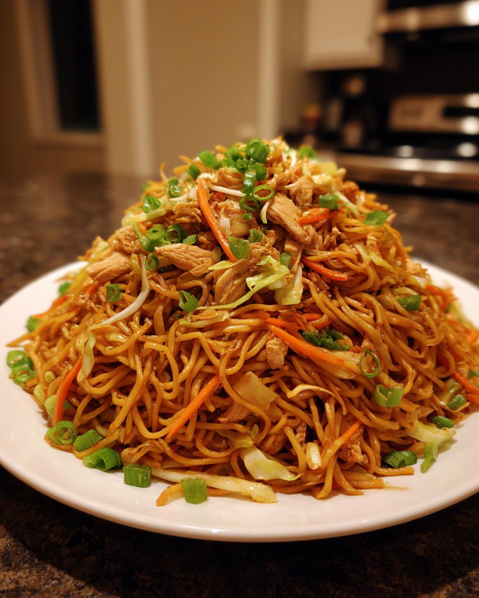 A large mound of homemade chicken chow mein recipe noodles mixed with shredded chicken, carrots, and cabbage, topped with green onions.