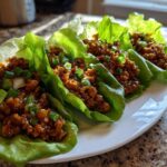 Four servings of savory chicken lettuce wraps filled with ground chicken mixture and topped with green onions.