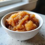 Close-up of chunky, homemade applesauce sprinkled with cinnamon served in a small white bowl.