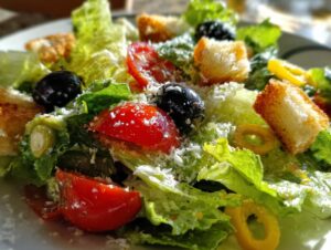 Close-up of a fresh copycat Olive Garden salad featuring romaine lettuce, tomatoes, black olives, pepperoncini, and grated Parmesan.