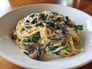 A close-up of creamy mushroom pasta featuring spaghetti tossed in a rich sauce with sautéed mushrooms and wilted spinach.