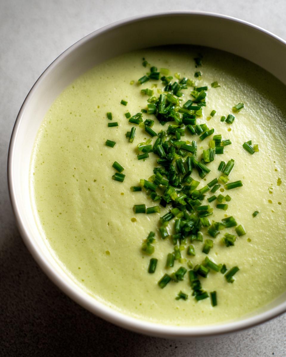 Close-up of a bowl of smooth, light green celery soup garnished generously with freshly chopped chives.