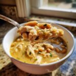 A spoonful of creamy white chicken chili, showing shredded chicken and white beans, lifted from a bowl.
