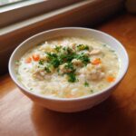 A comforting bowl of creamy chicken and rice soup, garnished with fresh parsley and visible carrots.