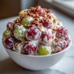 Close-up of a white bowl filled with creamy chicken salad chick grape salad, topped with pecans.
