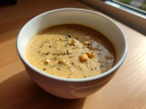 A close-up of a bowl of creamy chickpea soup, topped with whole chickpeas and dried herbs.