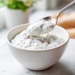 A spoonful of creamy coconut chia pudding being lifted from a white bowl, showing texture and chia seeds.