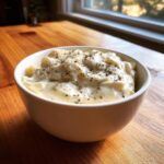 A close-up of thick, creamy homemade alfredo sauce topped with dried herbs in a white bowl.