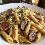 Close-up of creamy kielbasa pasta featuring penne noodles, sliced smoked sausage, and grated cheese.
