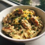 Close-up of creamy lemon chicken orzo pasta topped with fresh parsley and lemon zest in a white bowl.