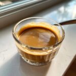 Close-up of creamy peanut sauce in a small glass ramekin, showing rich brown color and smooth texture.