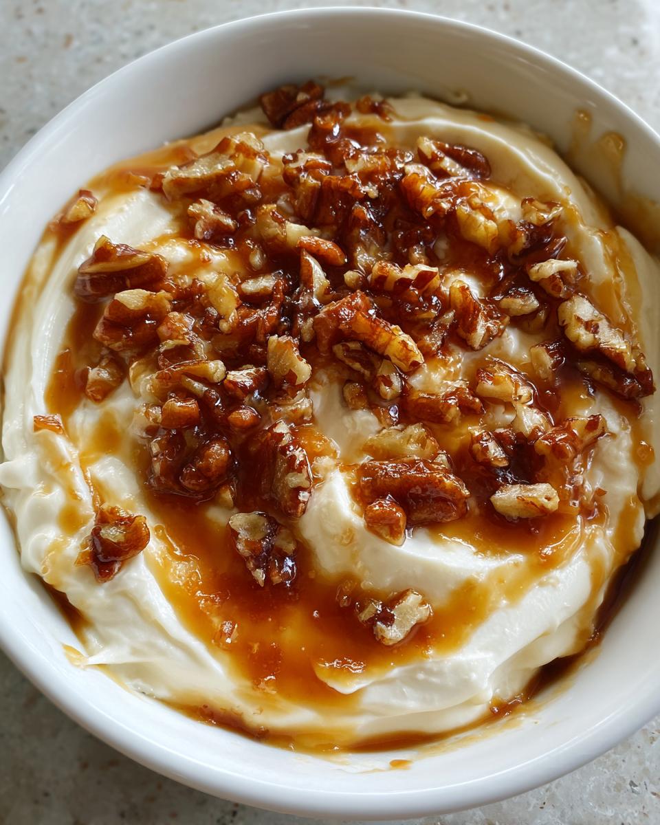 Close-up of a creamy pecan pie dip in a white bowl, drizzled with caramel sauce and topped with chopped pecans.