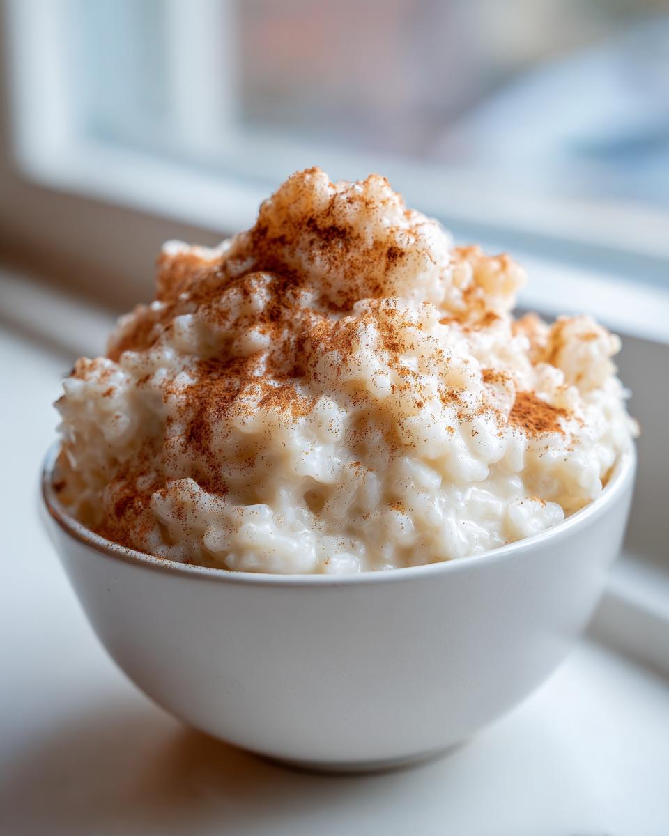 Close-up of creamy rice pudding served in a white bowl, generously sprinkled with cinnamon.