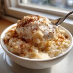 A spoonful of creamy rice pudding topped with whipped cream and sprinkled with cinnamon.