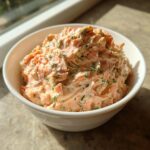 A close-up of creamy, pink salmon dip mixed with fresh dill, served in a white bowl.